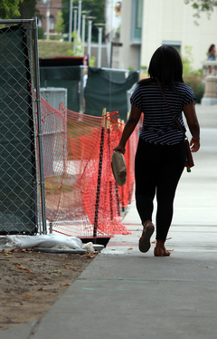 A woman walks along the sidewalk near some construction sites on the Syracuse University campus. Photo taken July 28, 2016
